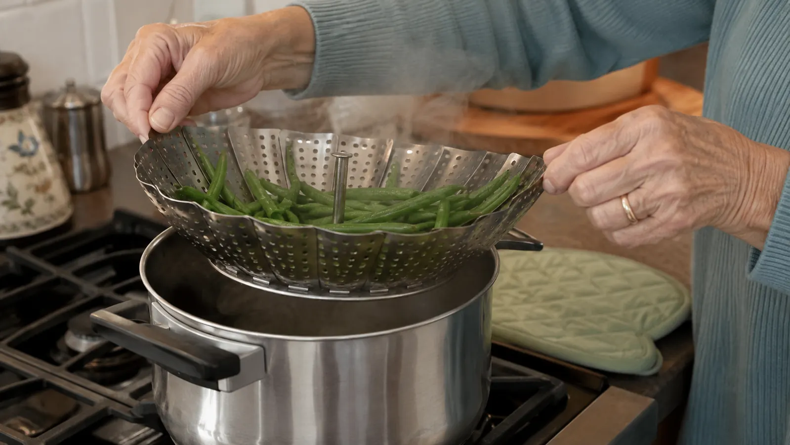 An older woman's hands lifting a metal collapsible steamer basket out of a saucepan of hot water on the stove