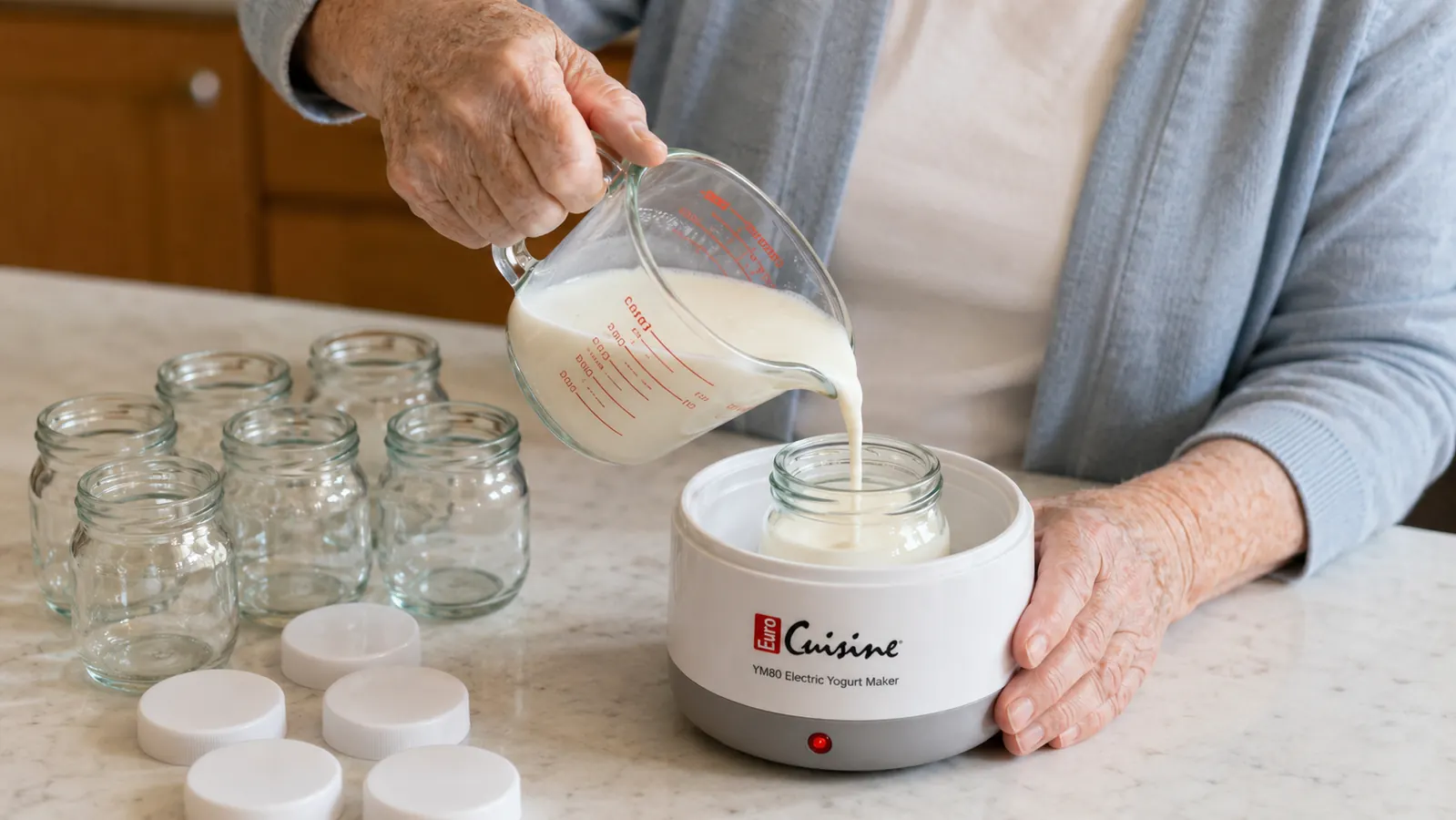 An older woman's hands pouring warm milk into a small glass jar set inside a white electric yogurt maker base