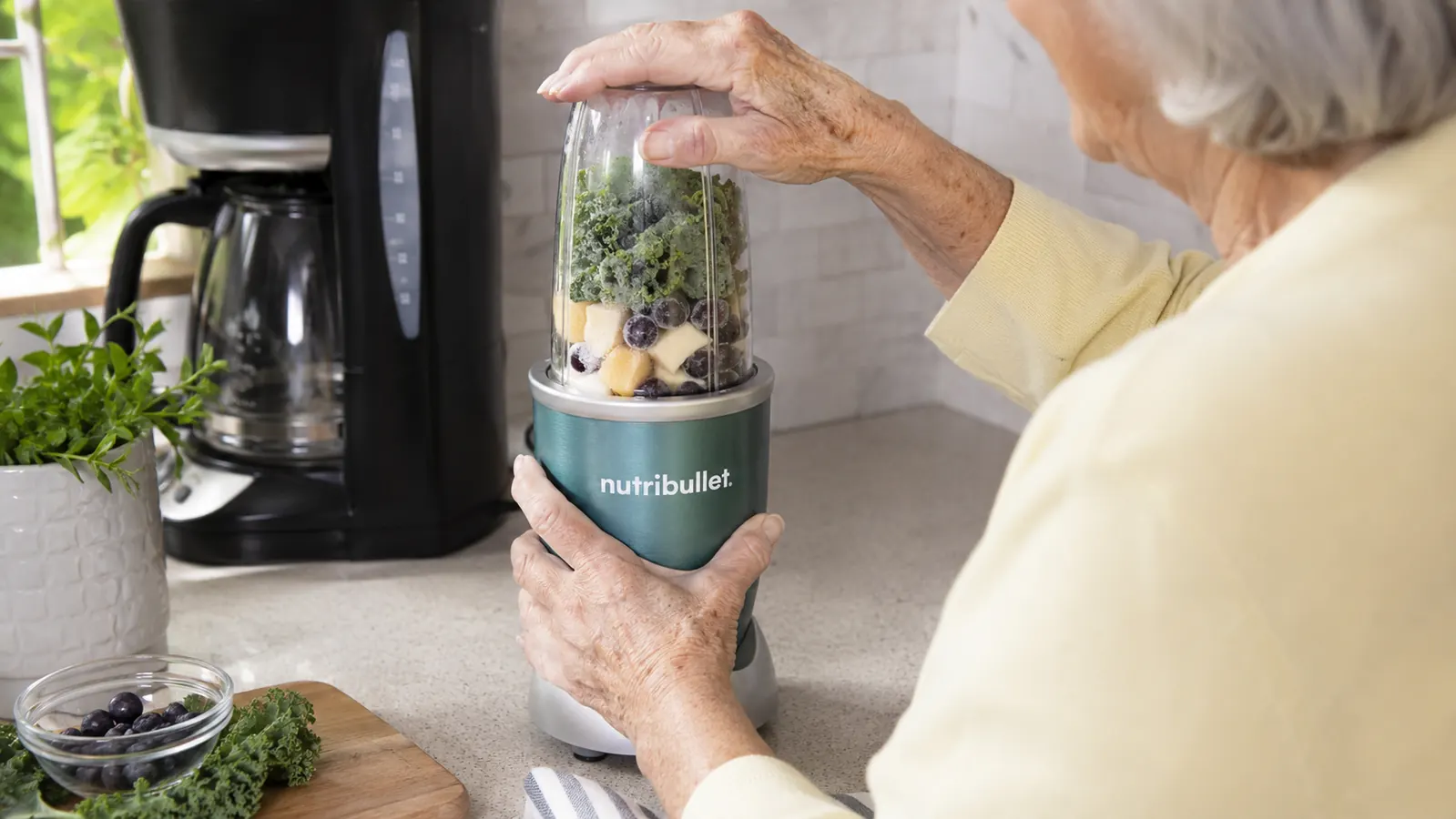 An older woman's hands twisting a personal blender cup onto its base on a kitchen counter